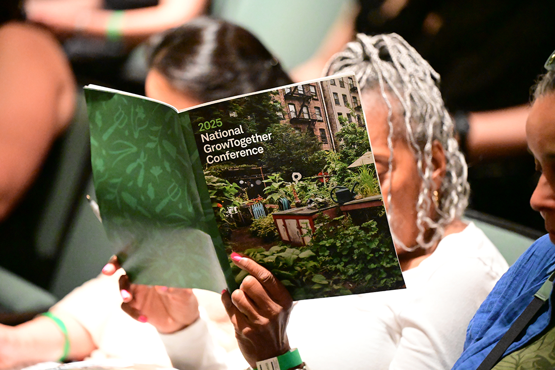 A close-up of a woman holding the 2025 National GrowTogether Conference program guide in front of her face while seated next to other people.